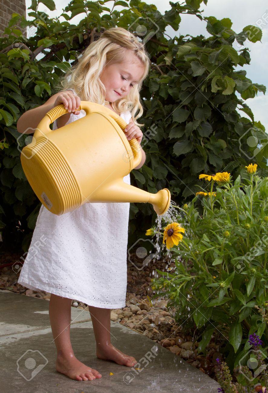 14416945-young-girl-stopping-to-smell-flowers-while-watering-them-Stock-Photo