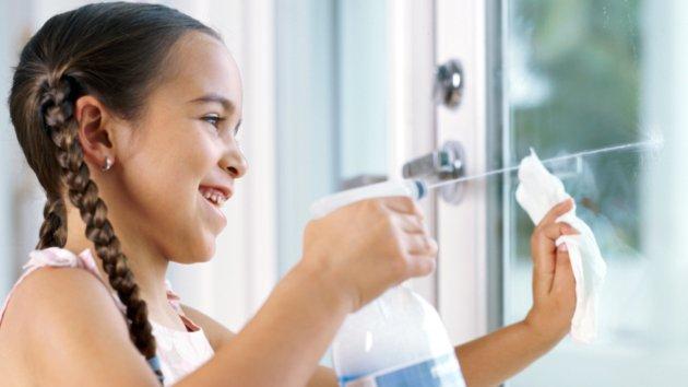 Girl (6-8) spraying cleaning product on window, smiling